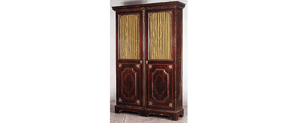 Une grande armoire en bois sombre, dotée de deux portes : la partie supérieure est recouverte de panneaux de tissu, la partie inférieure est ornée de panneaux de bois décoratifs.