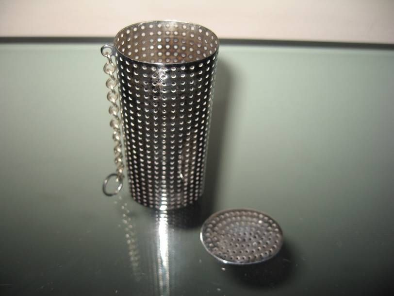 Une boule à thé en métal avec un corps cylindrique, un couvercle perforé amovible et une petite chaînette fixée sur le côté.
