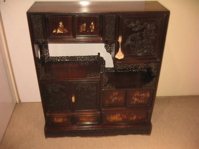 Une vitrine en bois sombre ornée de sculptures complexes, de multiples compartiments de rangement et de panneaux décoratifs incrustés.