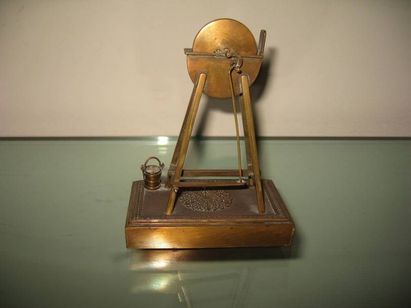 Une maquette miniature en laiton d'un puits avec un seau sur un socle, se détachant sur un fond clair uni.