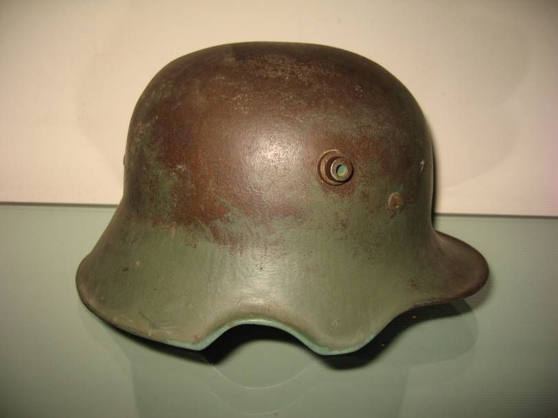 Un casque de combat allemand M1916 Stahlhelm en acier, avec un dôme rouillé et un bord inférieur verdâtre, vu de profil.