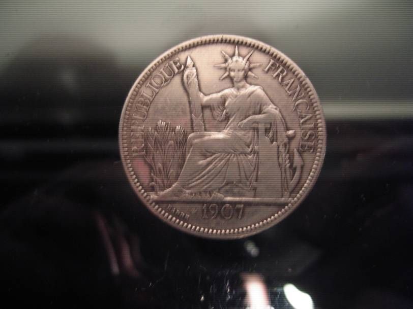 Pièce de monnaie de la République française de 1907 représentant un personnage assis, coiffé d'une couronne radieuse et tenant un faisceau de licteur, sur fond sombre.