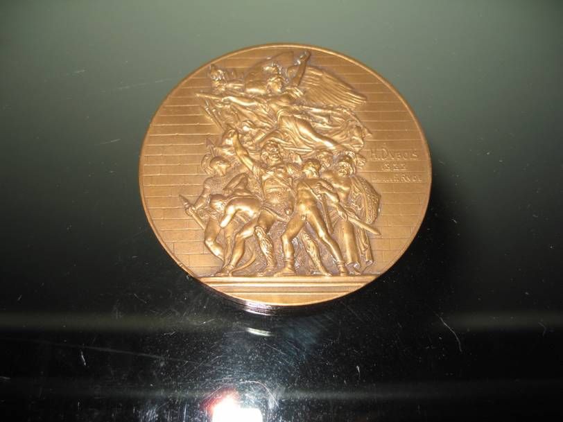 Médaille commémorative de couleur bronze ornée d'une scène sculptée en haut-relief représentant des personnages tenant des drapeaux et des armes.