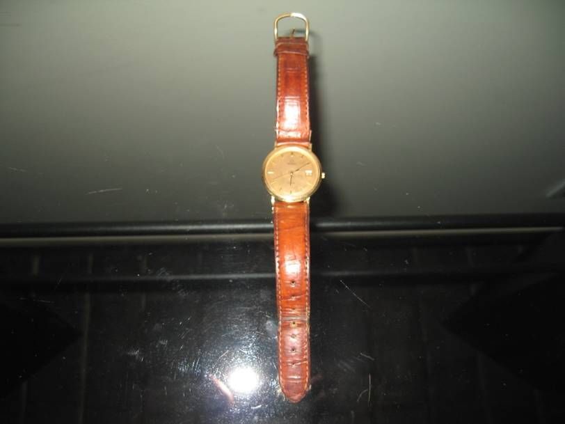 Une montre-bracelet en or avec un bracelet en cuir marron posée sur une surface noire.