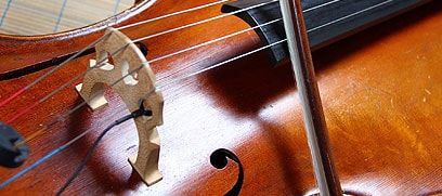 Gros plan sur le chevalet et les cordes d'un violon, avec un archet posé à proximité sur le corps en bois poli.