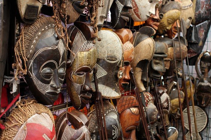 Une collection de masques africains en bois sculpté, aux textures, motifs et couleurs variés, est exposée dans une boutique.