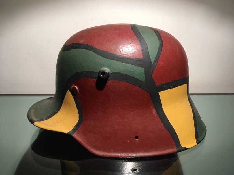 Vue latérale d'un casque en acier allemand de la Première Guerre mondiale, orné d'un motif de camouflage géométrique coloré rouge, vert et jaune.
