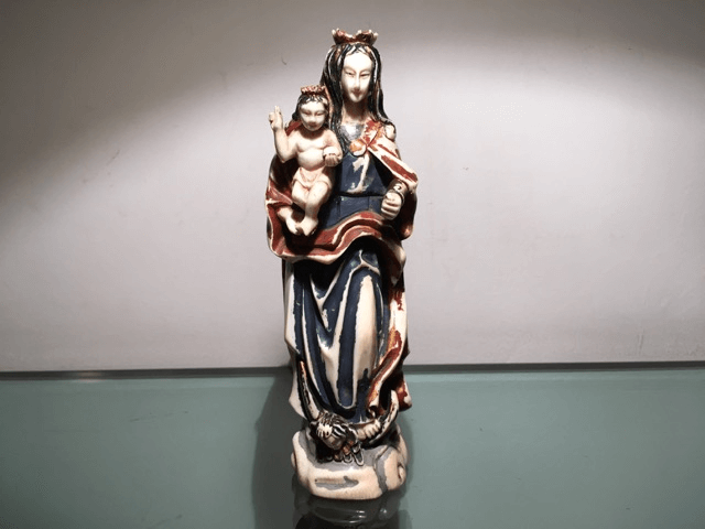 Petite figurine en céramique peinte à la main représentant une femme tenant un enfant, debout sur un serpent posé sur un socle circulaire.