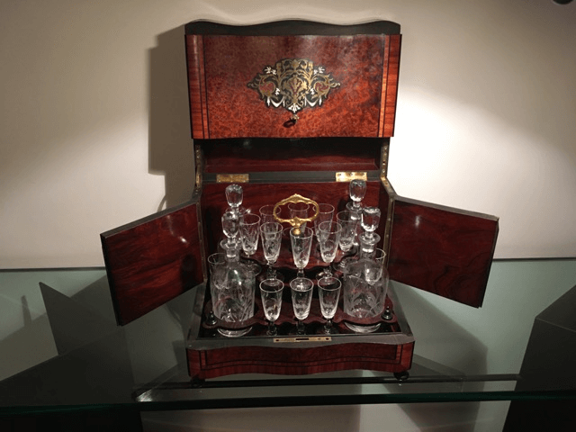 Un tantale ouvert en bois sombre, composé de carafes et de verres en cristal, présenté sur une table en verre.