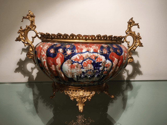 Un bol en céramique orné de motifs floraux bleus, rouges et blancs, doté de poignées en bronze doré et d'une base décorative.