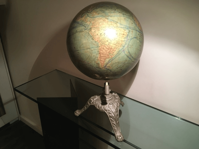 Un globe terrestre illuminé représentant les Amériques repose sur un trépied en métal orné, posé sur une console en verre.
