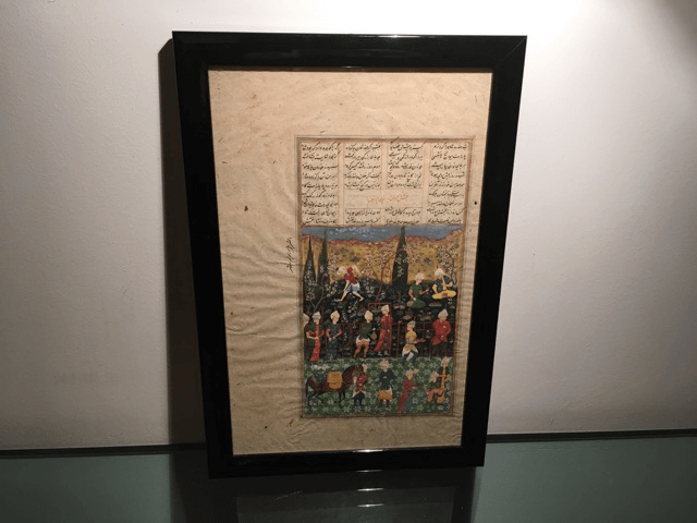 Une miniature persane encadrée représentant des personnages dans un paysage avec des arbres stylisés au-dessus de lignes de calligraphie arabe.