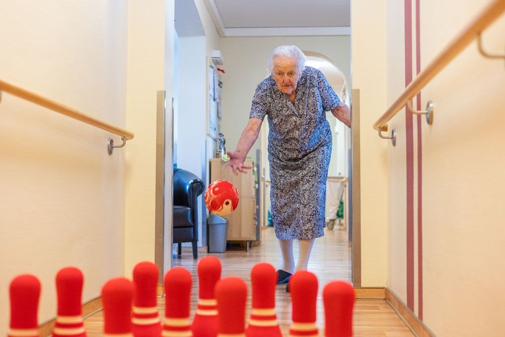Eine ältere Frau spielt in einem Flur eine Partie Bowling.