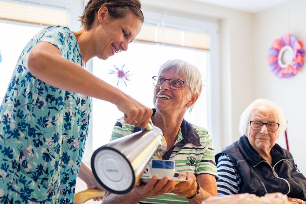 Eine Krankenschwester gießt einer älteren Dame Tee in eine Tasse.