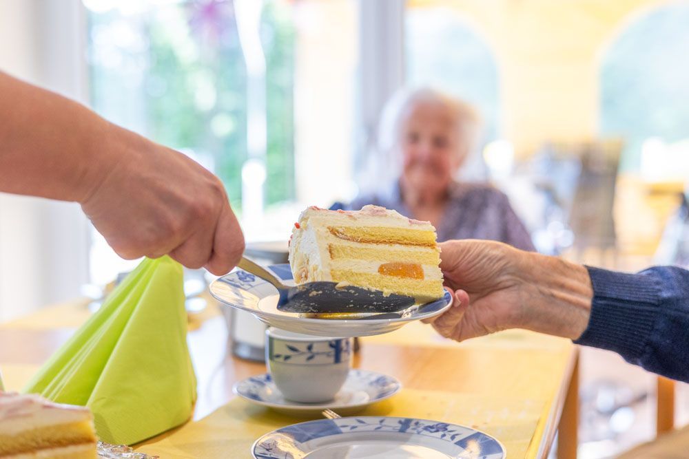 Eine Frau serviert einer älteren Frau an einem Tisch ein Stück Kuchen.