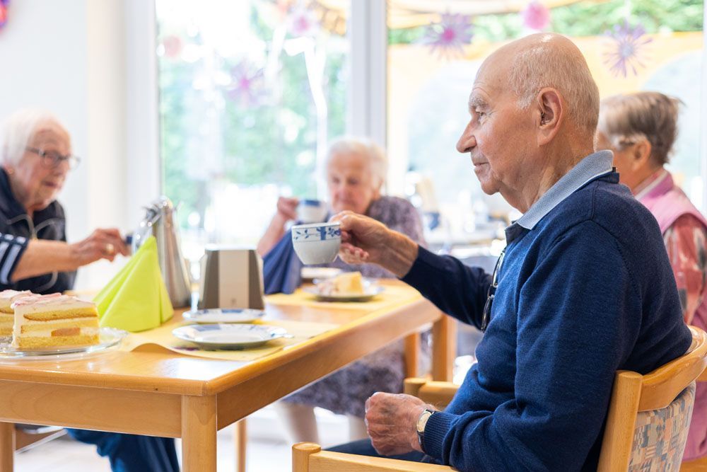 Ein älterer Mann sitzt an einem Tisch und trinkt eine Tasse Kaffee.