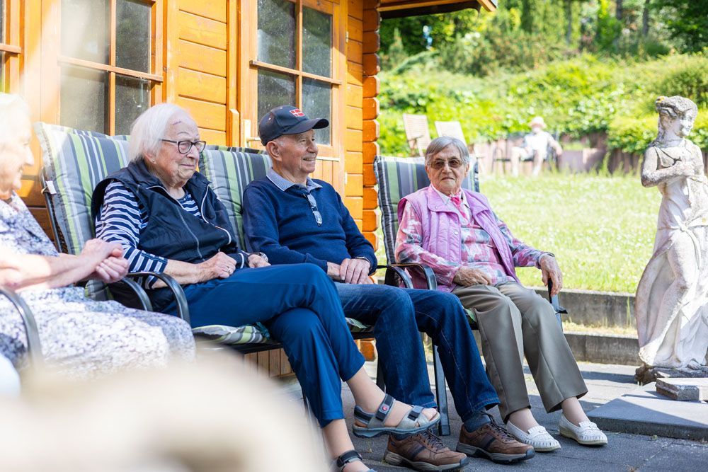 Eine Gruppe älterer Menschen sitzt auf Stühlen vor einem Haus.