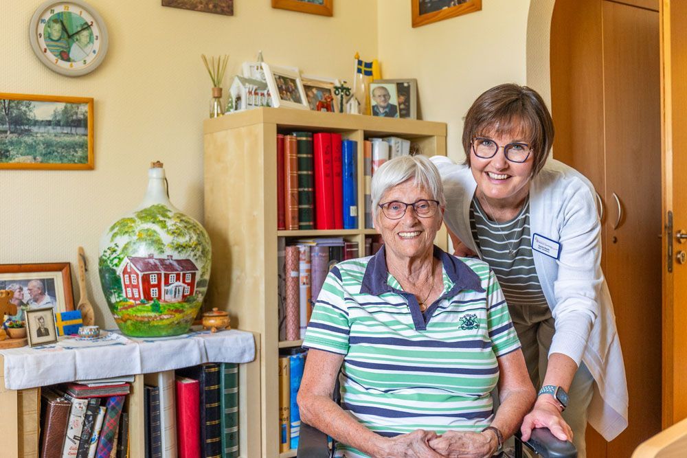 Eine Frau steht neben einer älteren Frau im Rollstuhl.