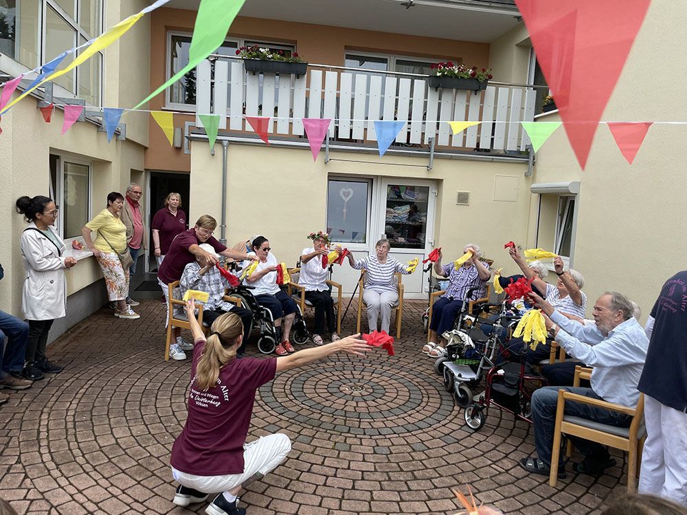 Eine Gruppe von Leuten sitzt auf Stühlen auf einer gemauerten Terrasse.