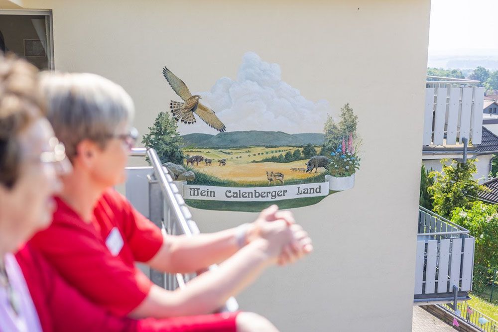 Zwei Frauen sitzen auf einem Balkon mit einem Gemälde an der Wand.