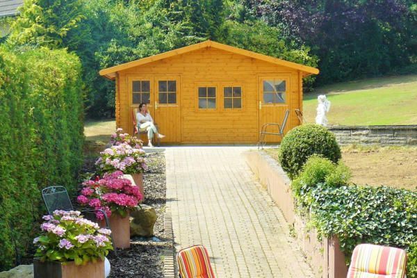 Eine Frau sitzt auf einer Bank vor einem Holzhaus.