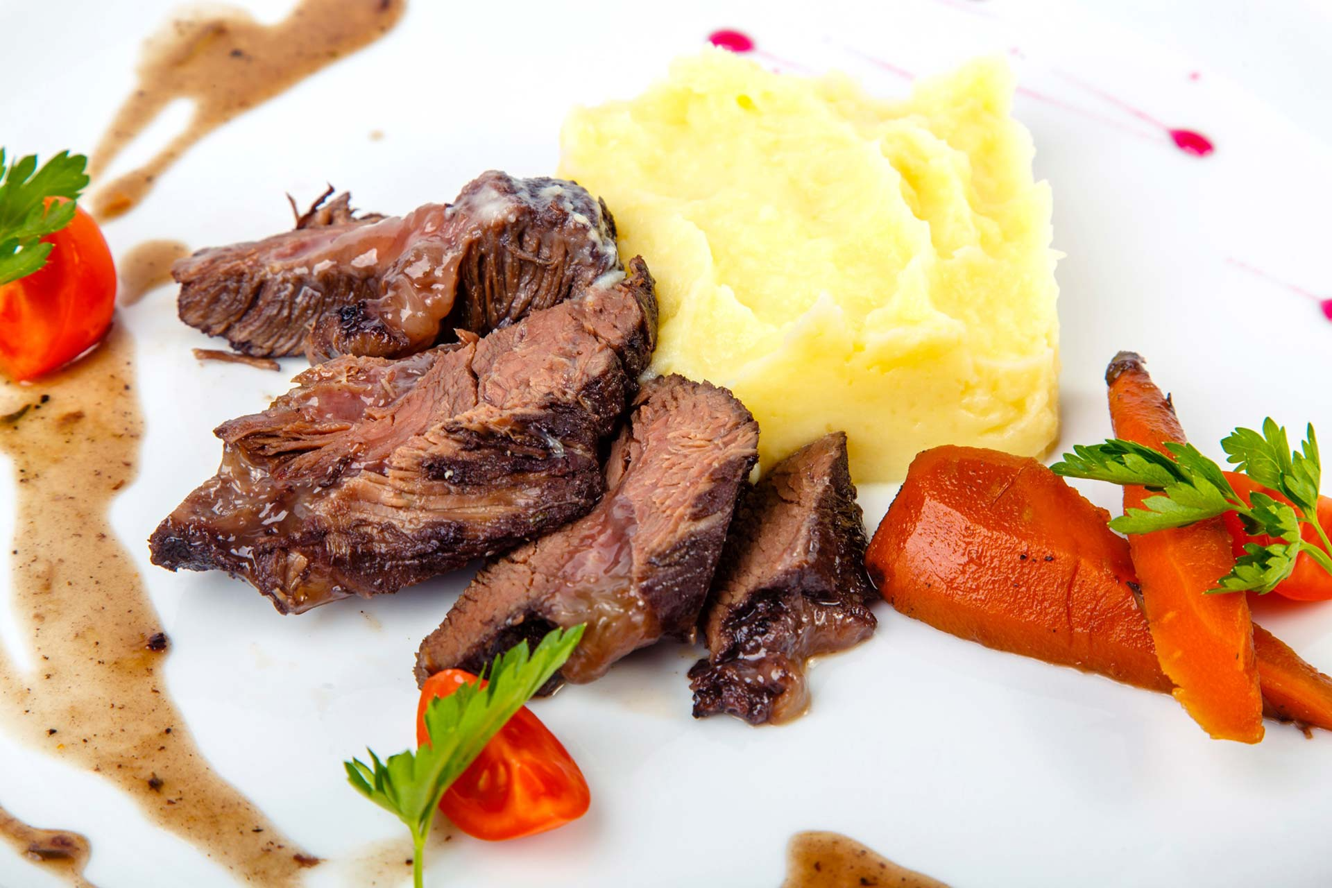 Un plato blanco cubierto con carne, puré de papas, zanahorias y tomates.