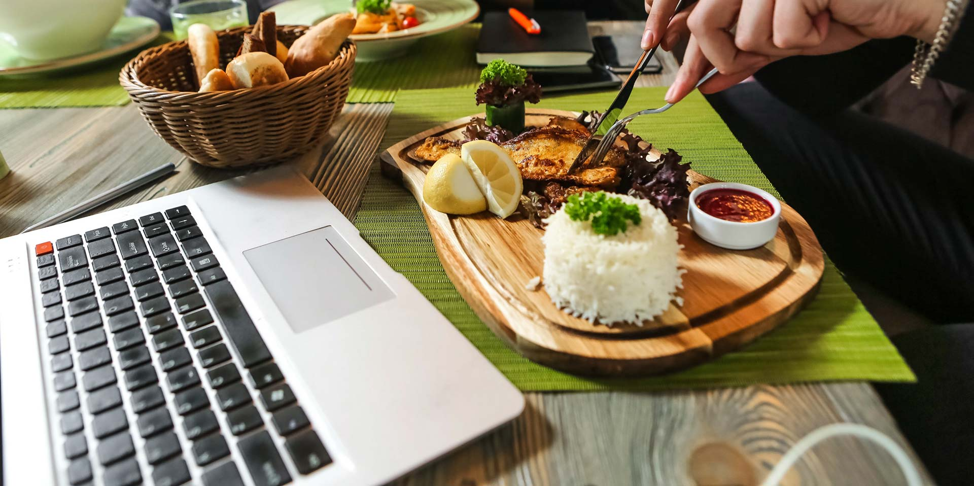 Una persona está sentada en una mesa con una computadora portátil y un plato de comida.