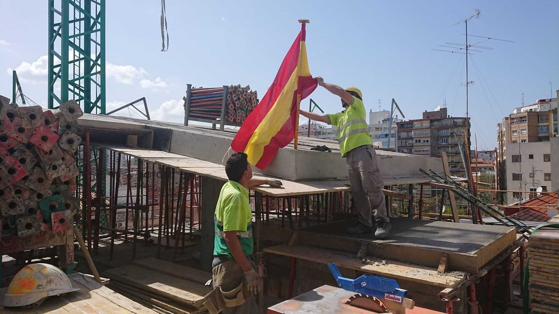 Dos trabajadores de la construcción ondean una bandera en la parte superior de un edificio en construcción.