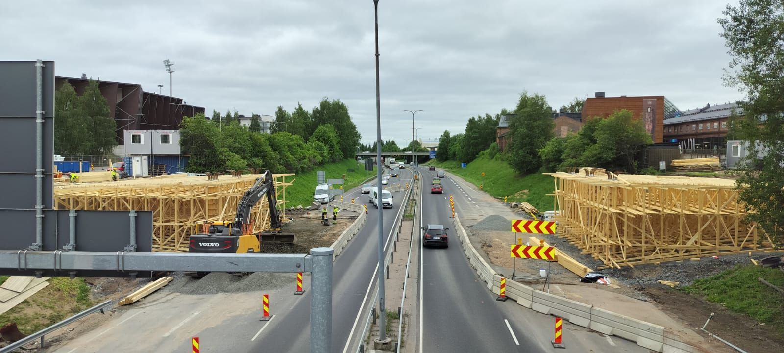 Tienrakennustyöt moottoritien eritasoliittymässä, jossa liikennettä, kaiteita ja rakennusmateriaaleja on molemmin puolin.