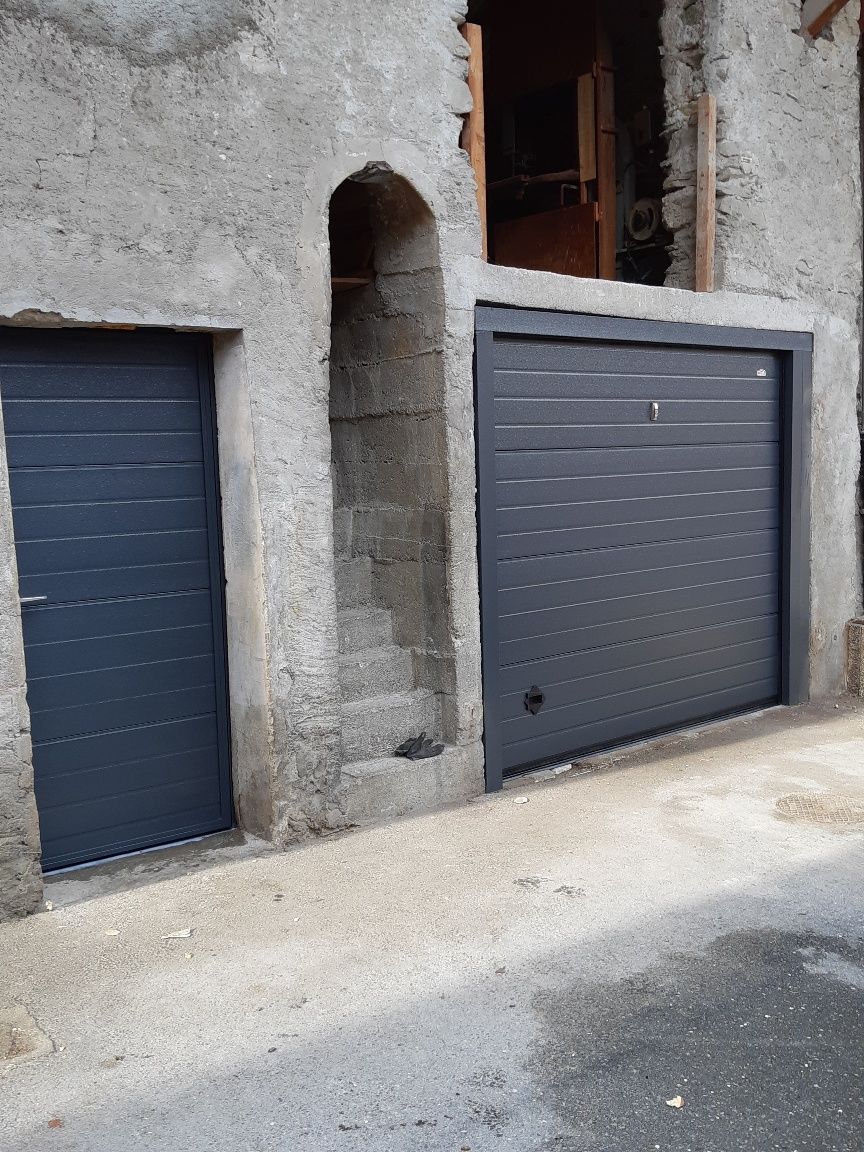 Old stone wall with two dark garage doors and a narrow arched opening between them