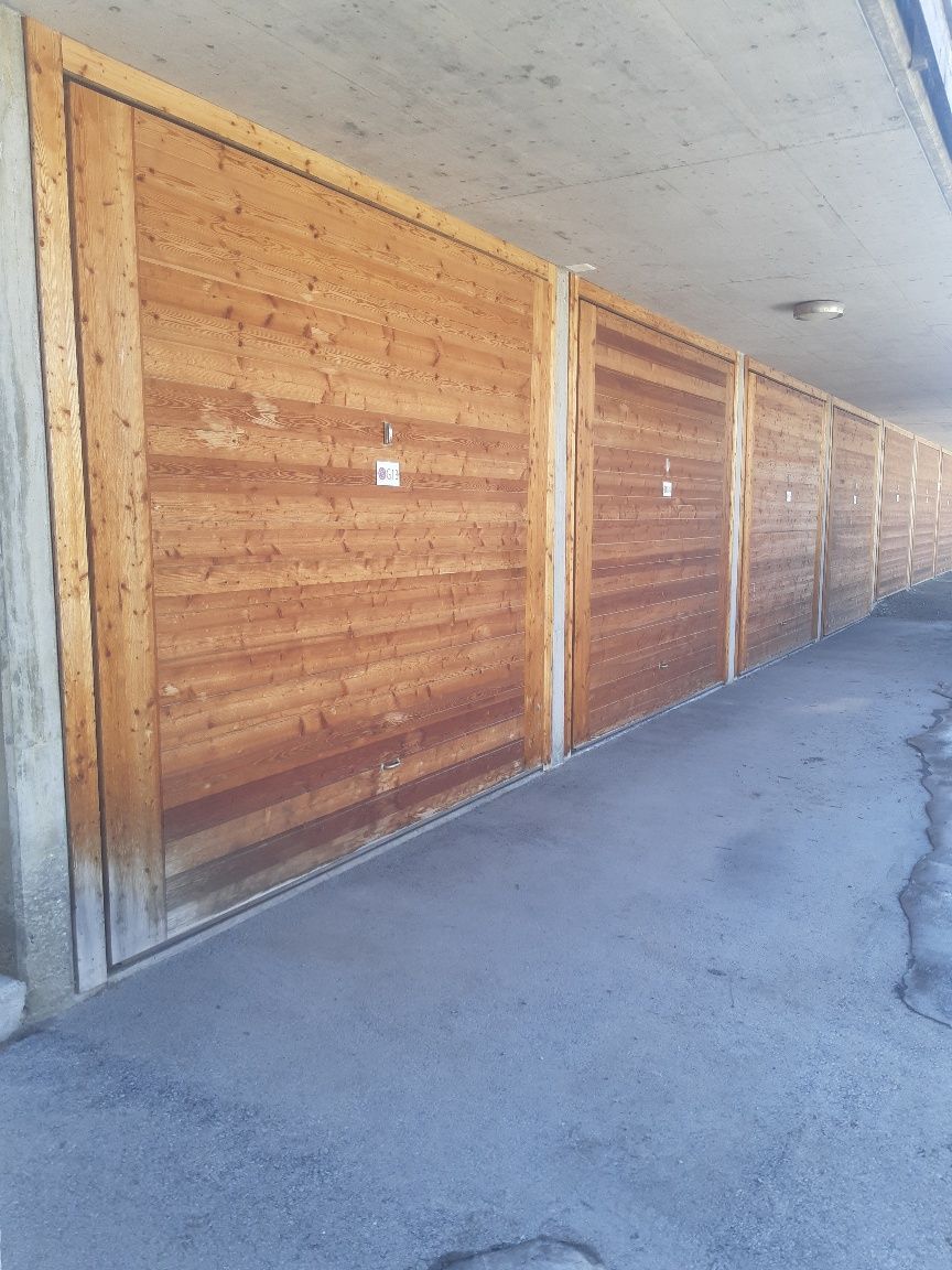 Une rangée de portes de garage en bois longe une allée en béton sous un auvent.