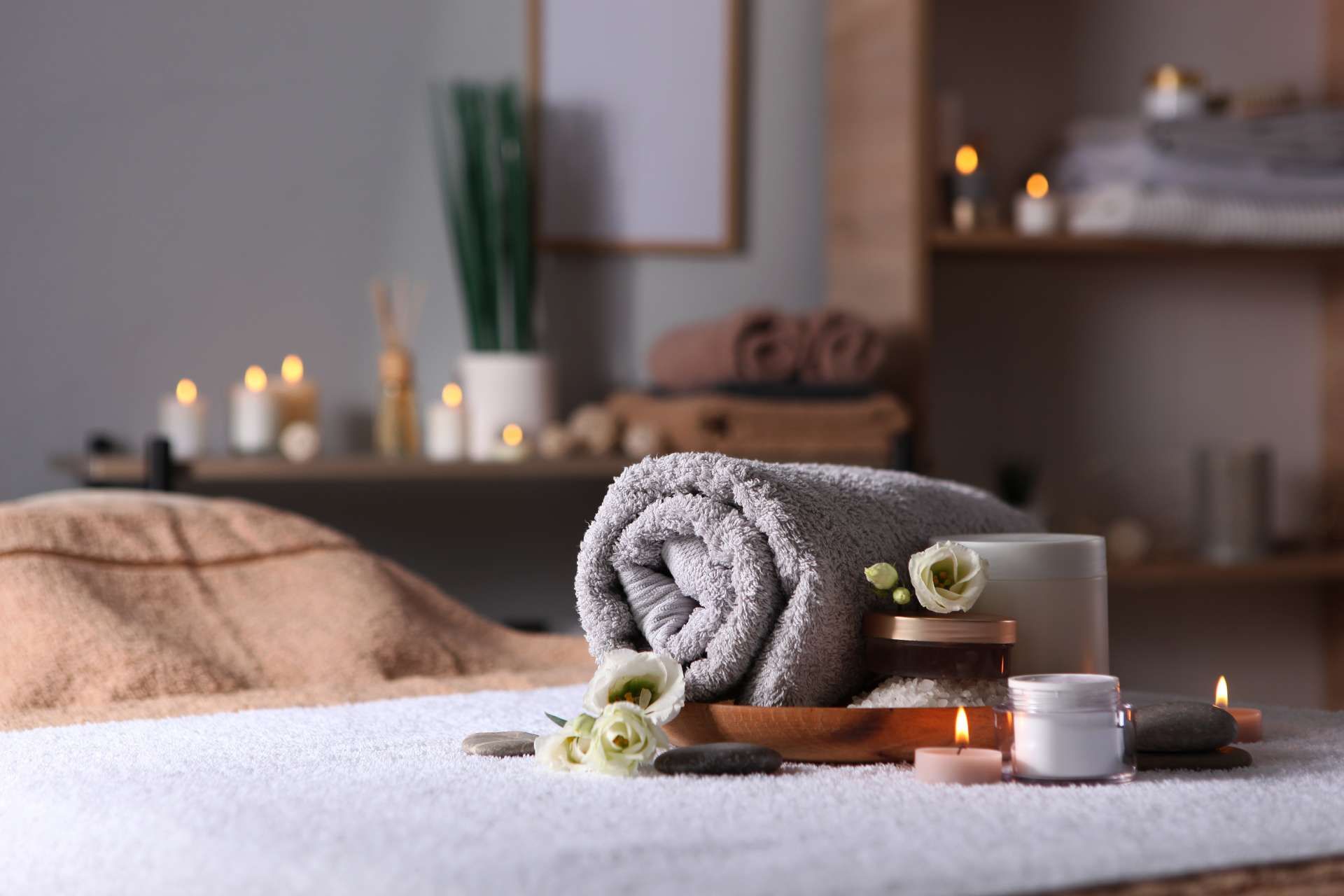 Ambiance spa avec serviette roulée, fleurs, bougies et bocaux sur une table de massage.