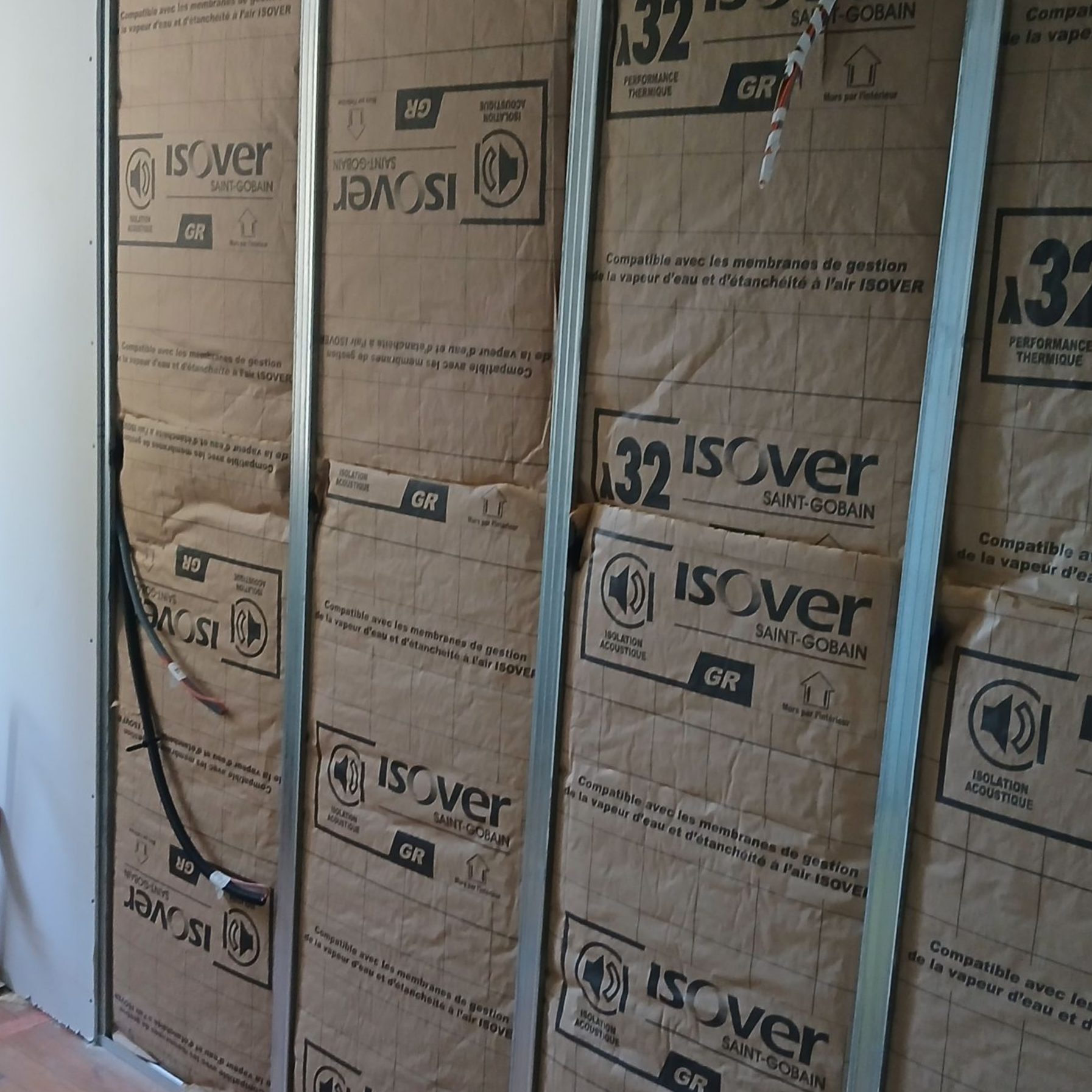 Personne installant de l'isolant sur un mur à l'aide de montants métalliques.