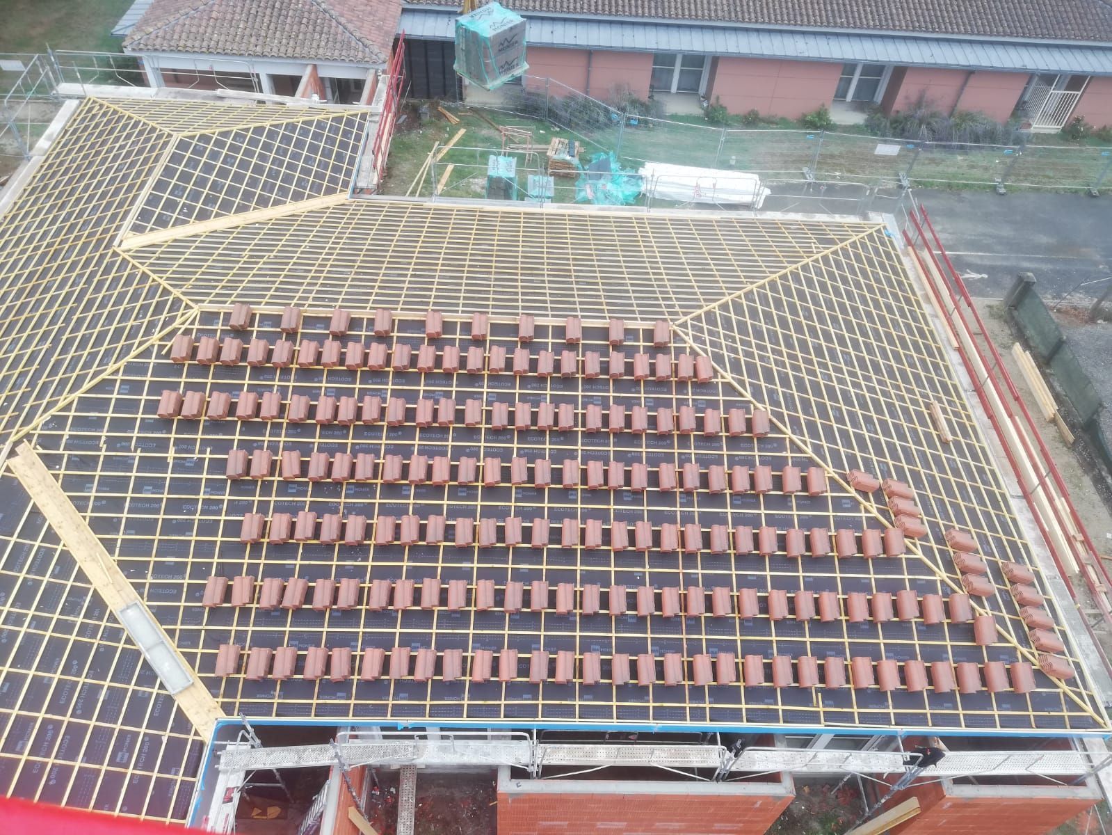 Toiture en tuiles de terre cuite avec gouttière contre un bâtiment en pierre et béton.