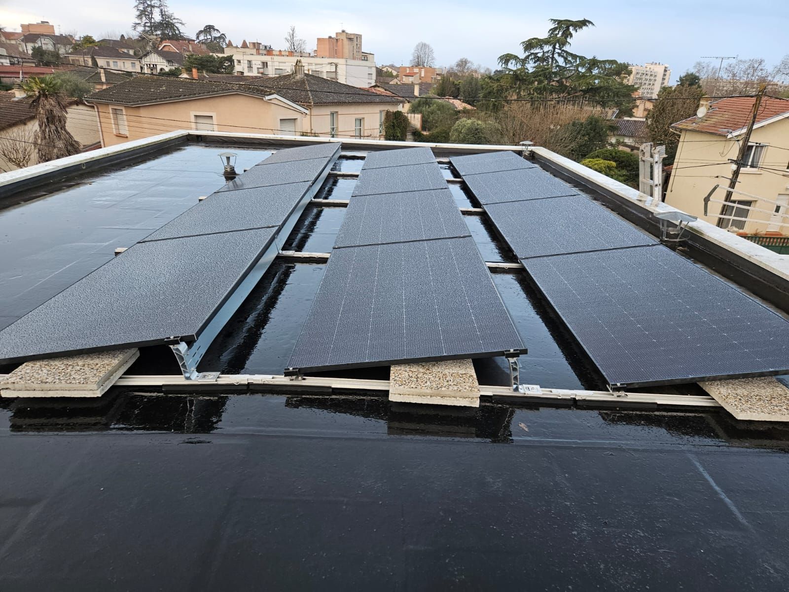 Panneaux solaires sur un toit résidentiel contre un ciel bleu avec des nuages.