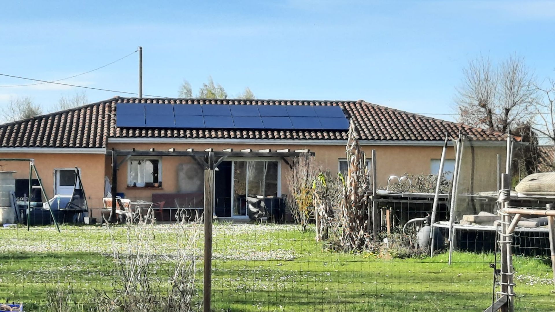 Maison avec panneaux solaires sur le toit, située dans une cour avec une pelouse verte et un ciel bleu.