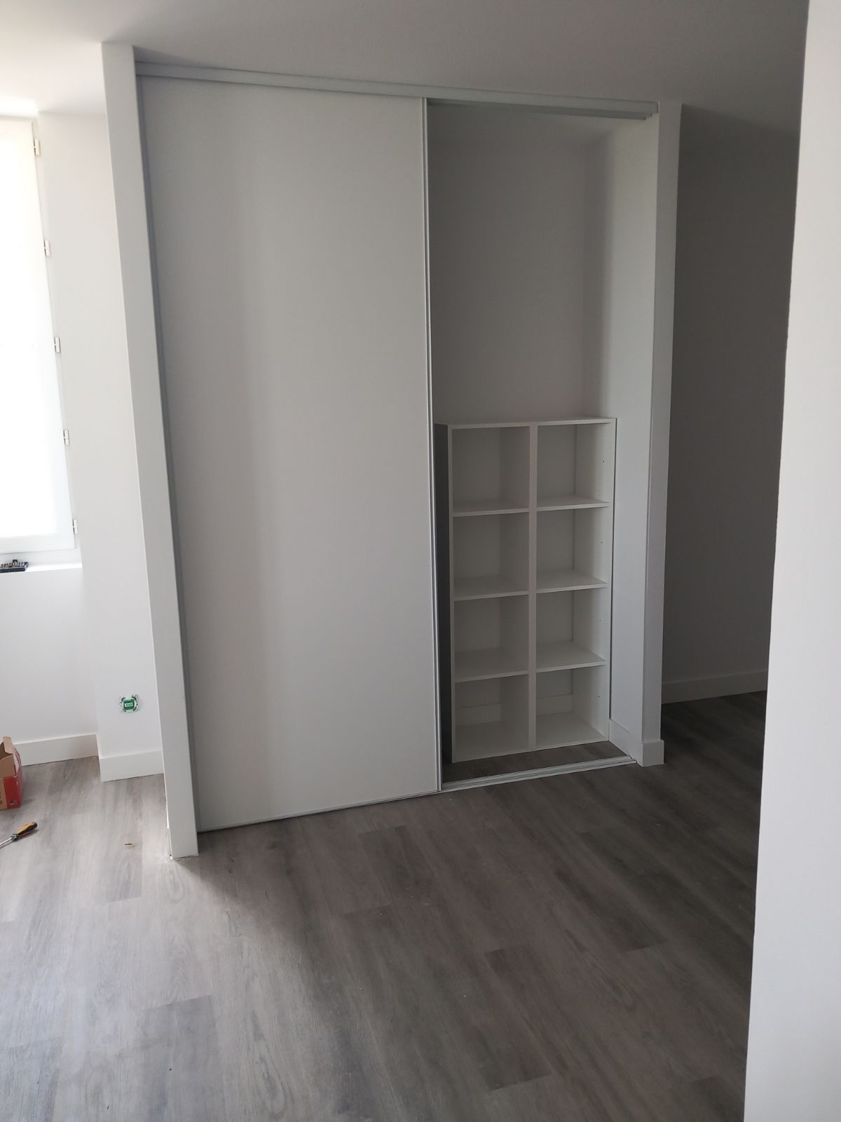 Placard à portes coulissantes blanches avec étagères intégrées ; sol gris.
