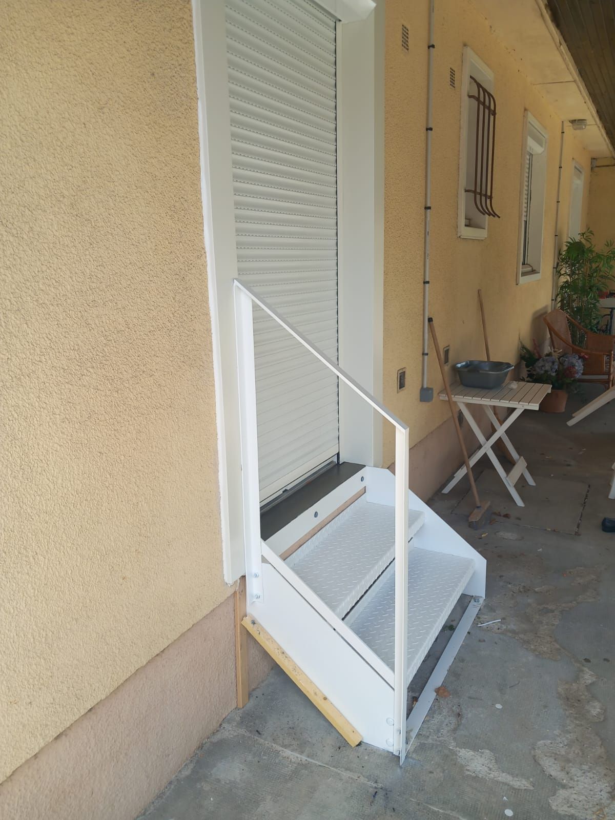 Escalier extérieur blanc menant à une porte avec un volet blanc fermé.