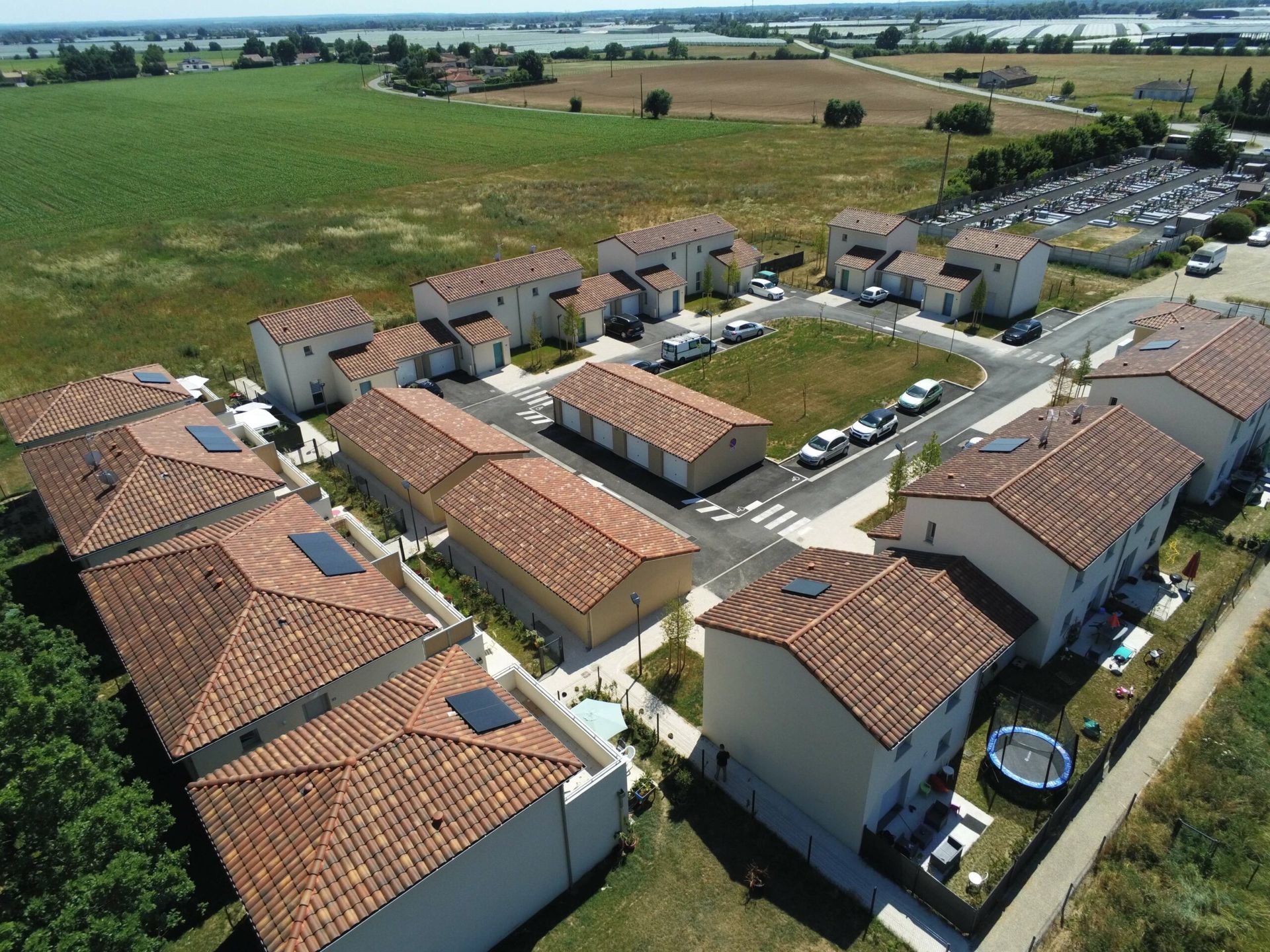 Vue aérienne d'un quartier résidentiel aux toits en terre cuite, entouré de champs et d'un parking.