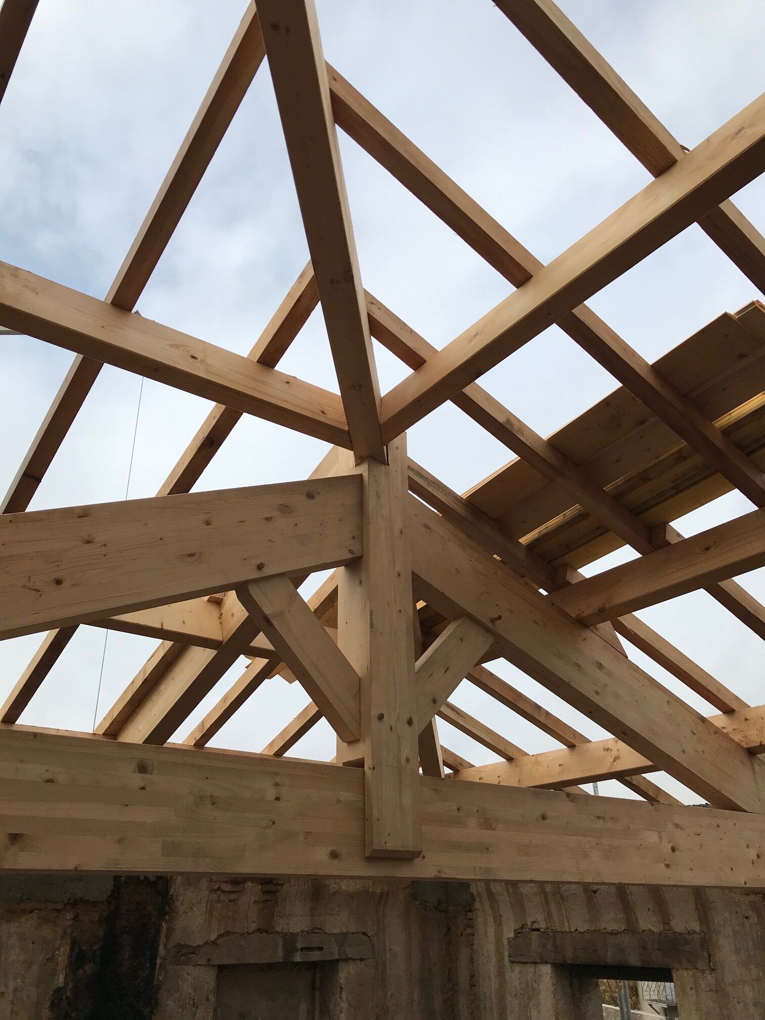 Poutres en bois d'une structure de toit en cours de construction, sur fond de ciel nuageux.