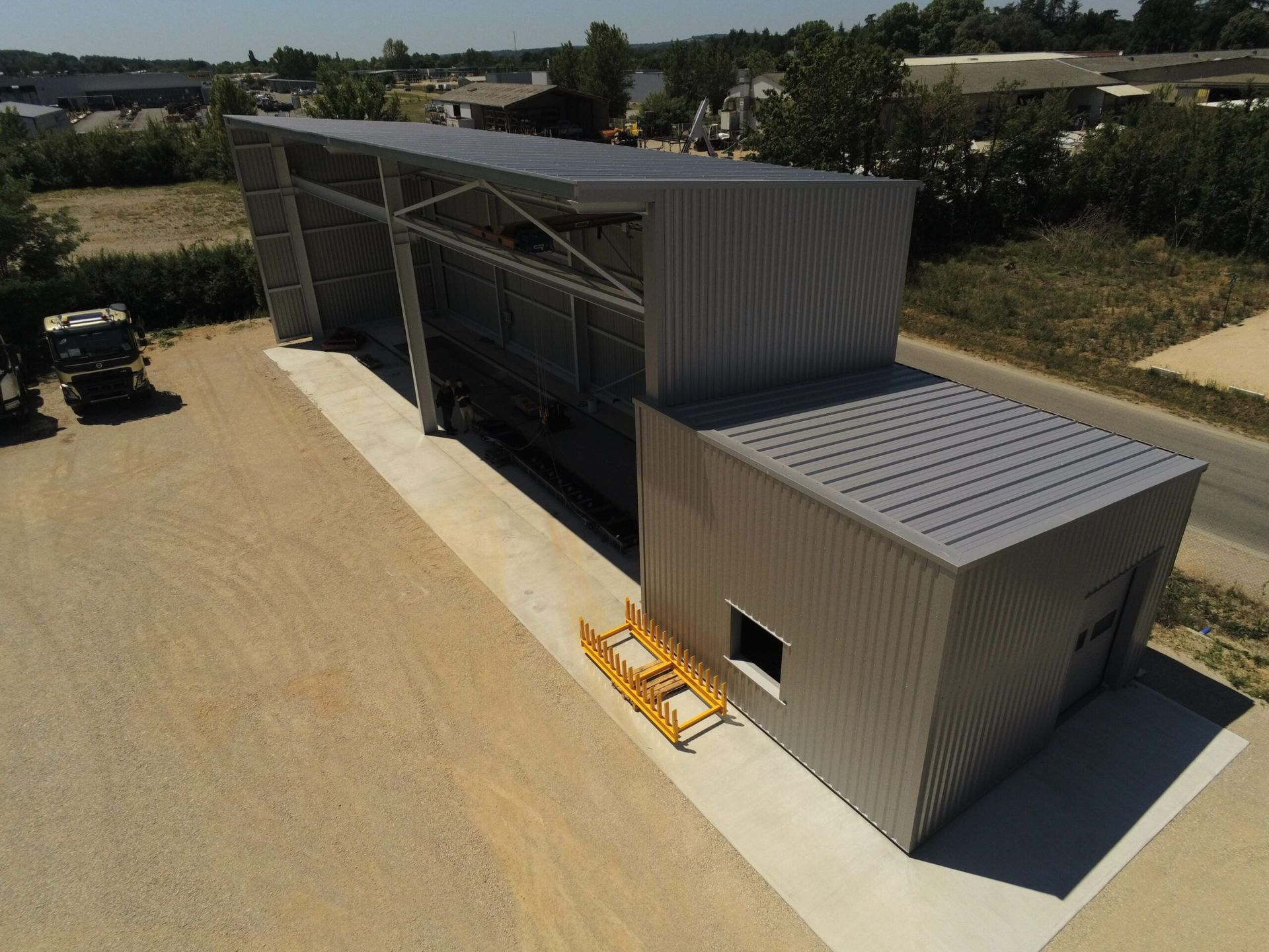 Bâtiment industriel métallique avec panneaux solaires, longue passerelle et barrière de sécurité jaune.