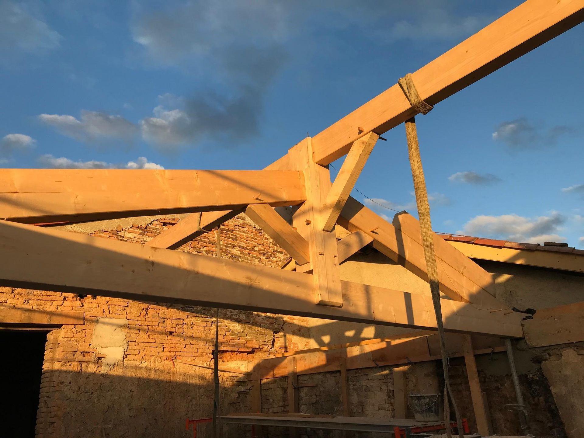 Charpente de toit en bois en construction contre un ciel partiellement nuageux.