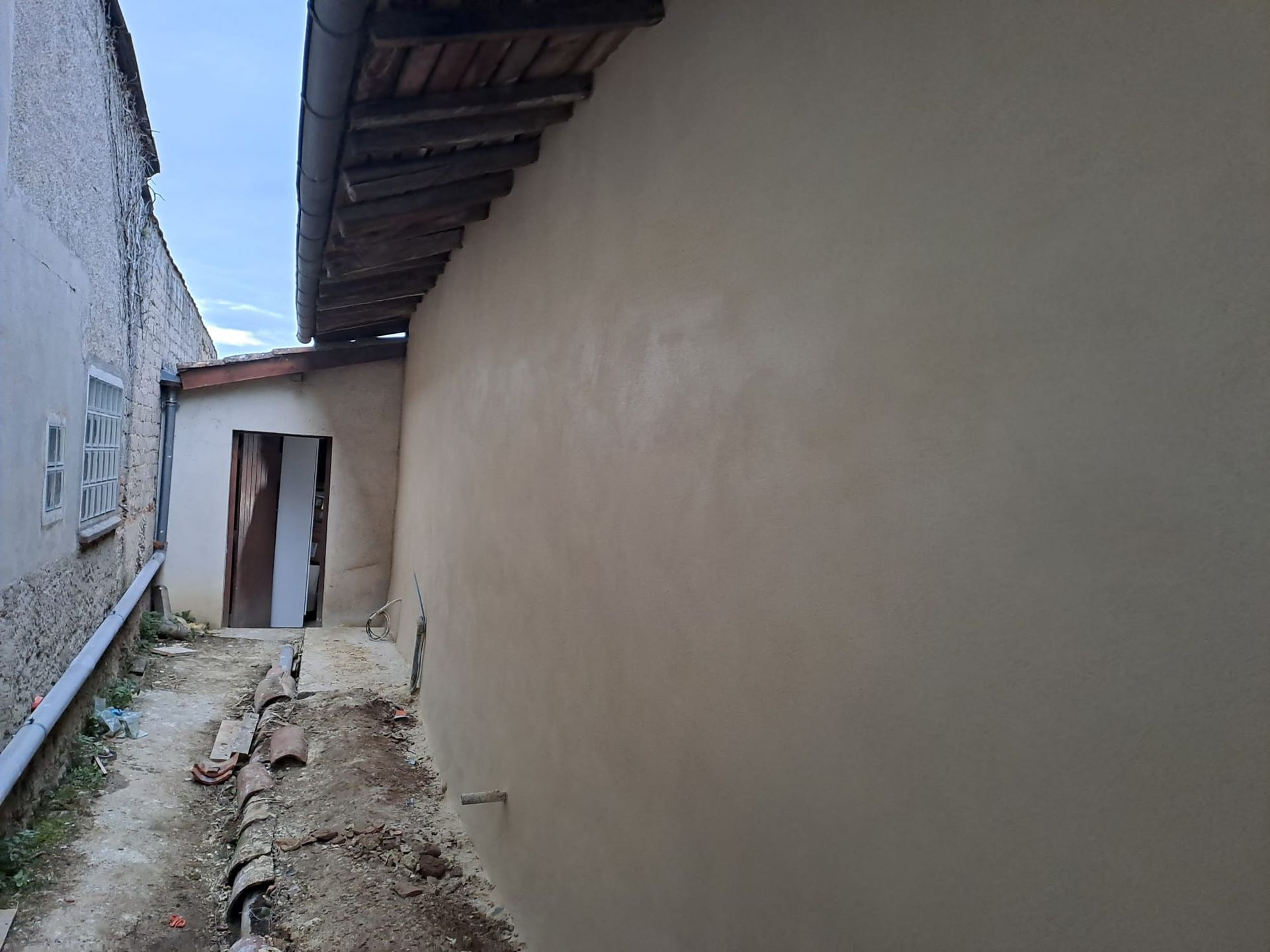 Ruelle étroite avec mur beige fraîchement enduit, porte et vieux bâtiments.