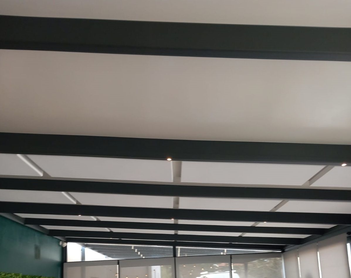 Plafond avec poutres sombres et panneaux blancs, avec un mur vert visible à gauche.