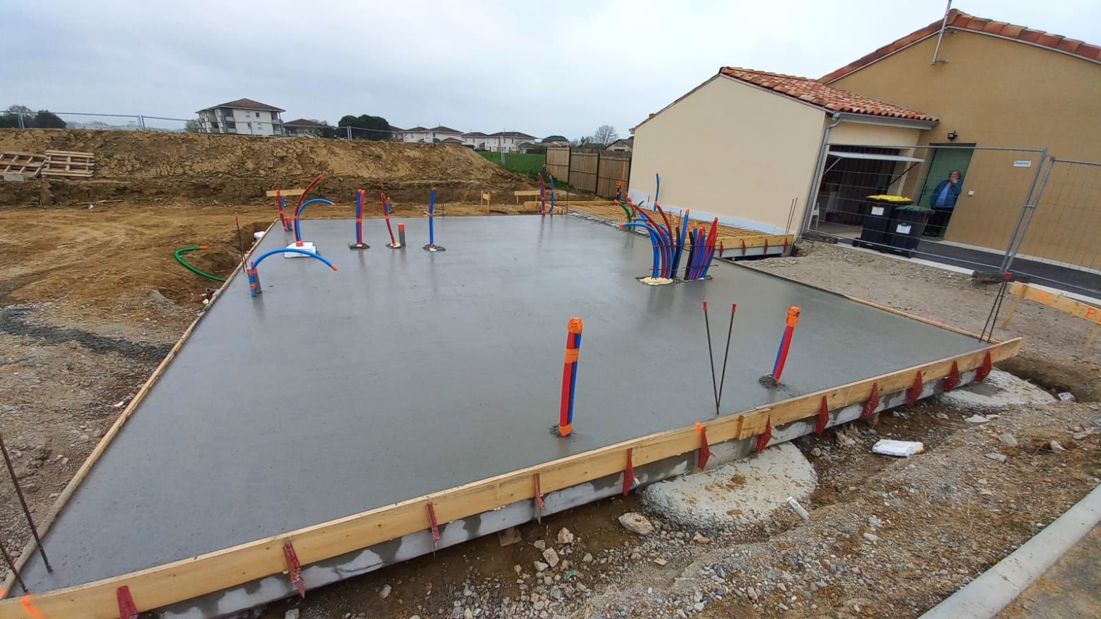 Fondation en béton fraîchement coulée avec tuyaux de plomberie, bâtiment en construction à l'extérieur.