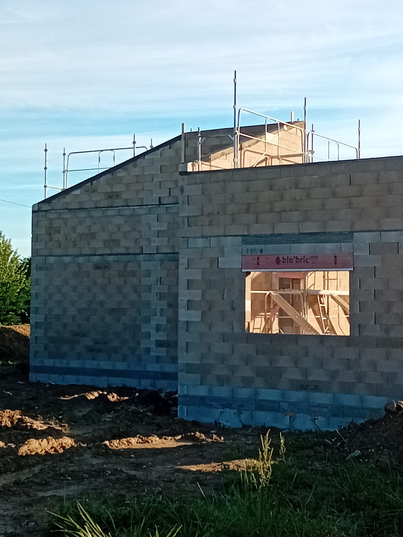 Construction d'un bâtiment avec murs en parpaings ; échafaudage ; châssis de fenêtre. Ciel nuageux.