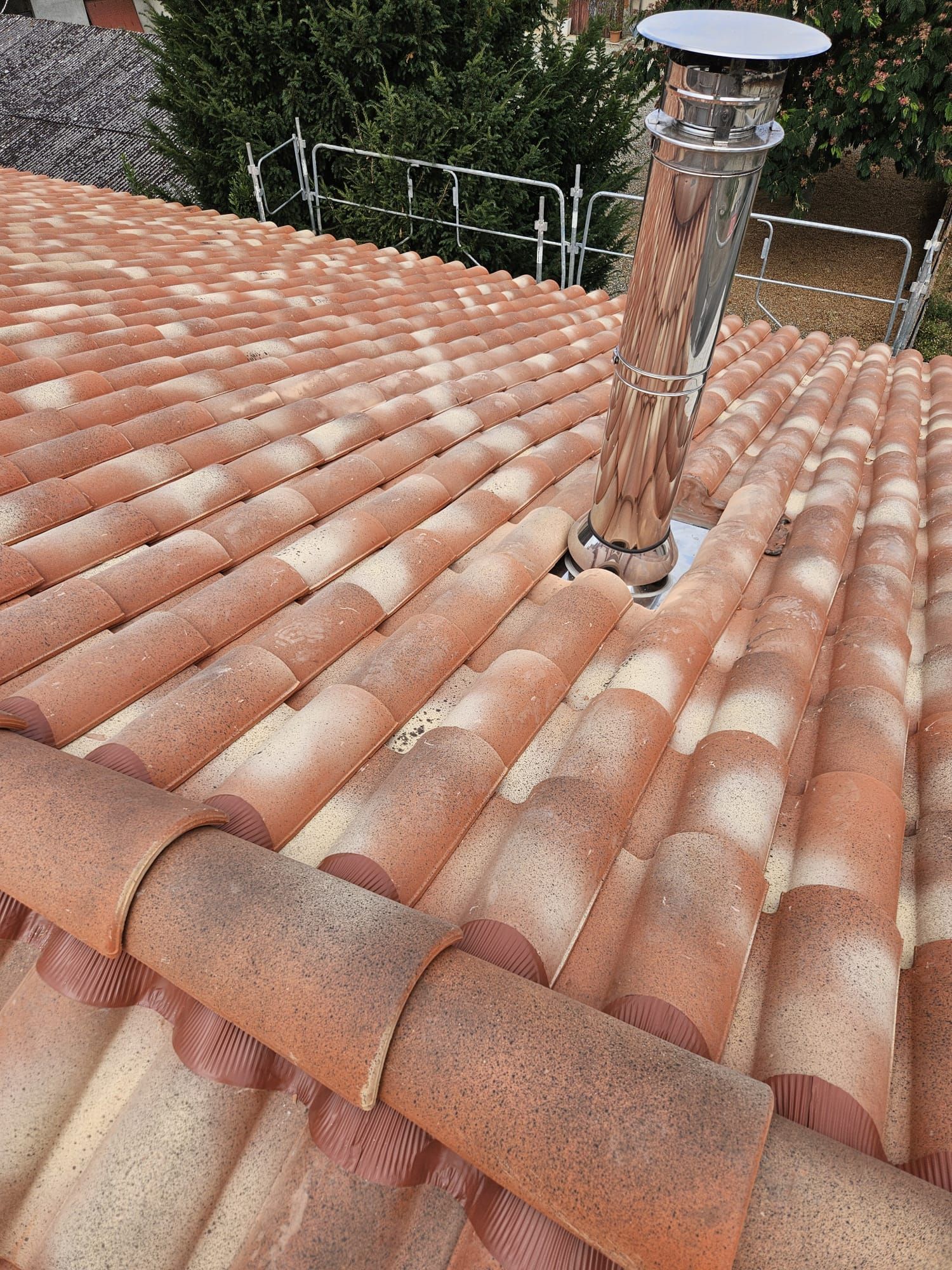 Toit en tuiles rouges avec une cheminée en métal brillant.