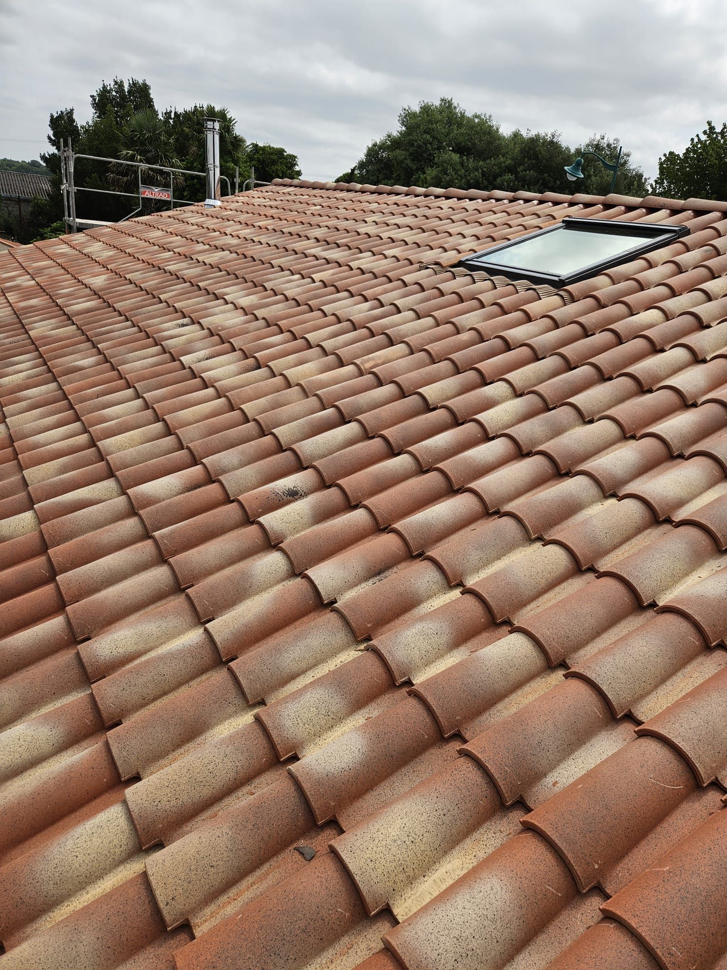 Toiture en tuiles rouges avec gouttière en métal et mur en briques.