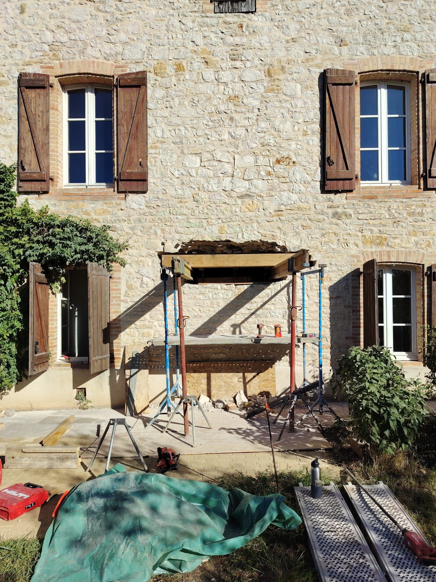 Façade d'un bâtiment en pierre en construction avec échafaudage. Trois fenêtres, volets marron et outils.