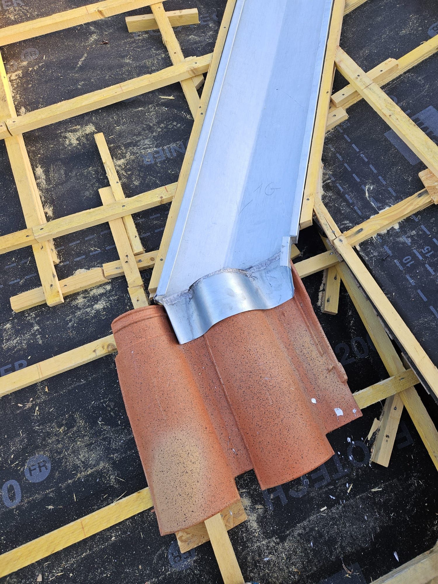 Toiture : tuiles en terre cuite et solins argentés rencontrent une gouttière métallique ; chantier.